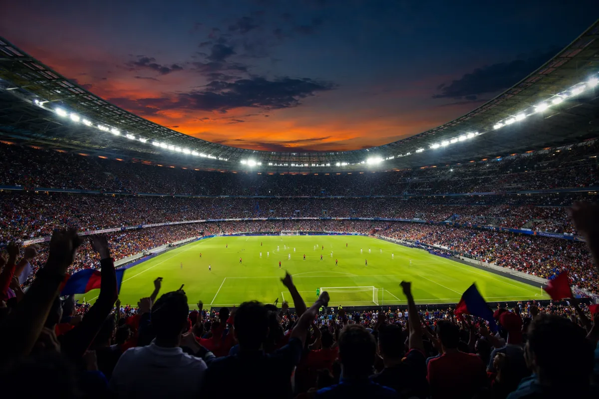 A wide shot of a professional football stadium at dusk, bright floodlights illuminating th