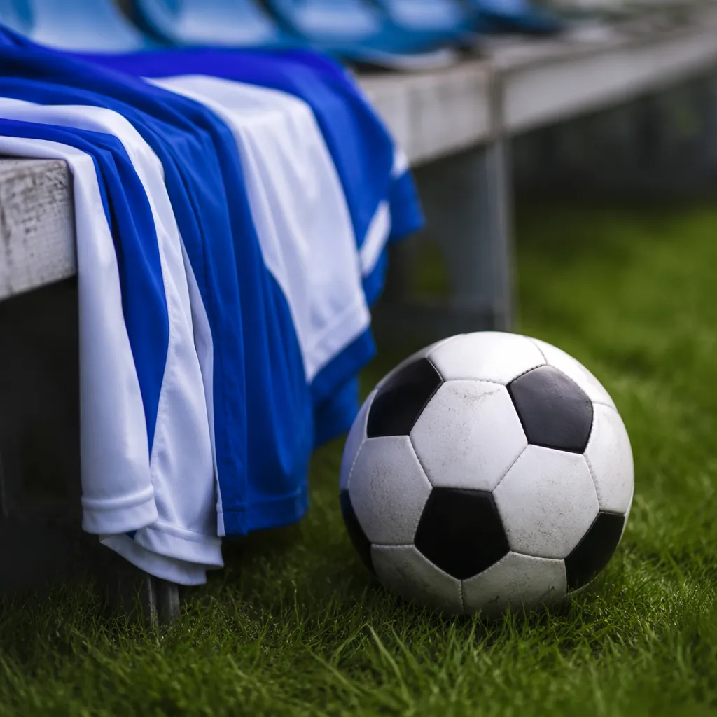 Close-up of a football on a green grass pitch, blue and white team jersey draped