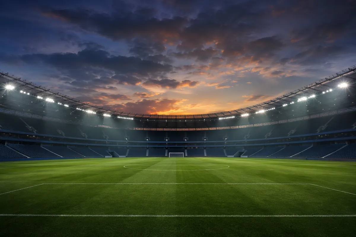 Wide shot of a generic football stadium at dusk, empty green pitch, bright floodlights, mo