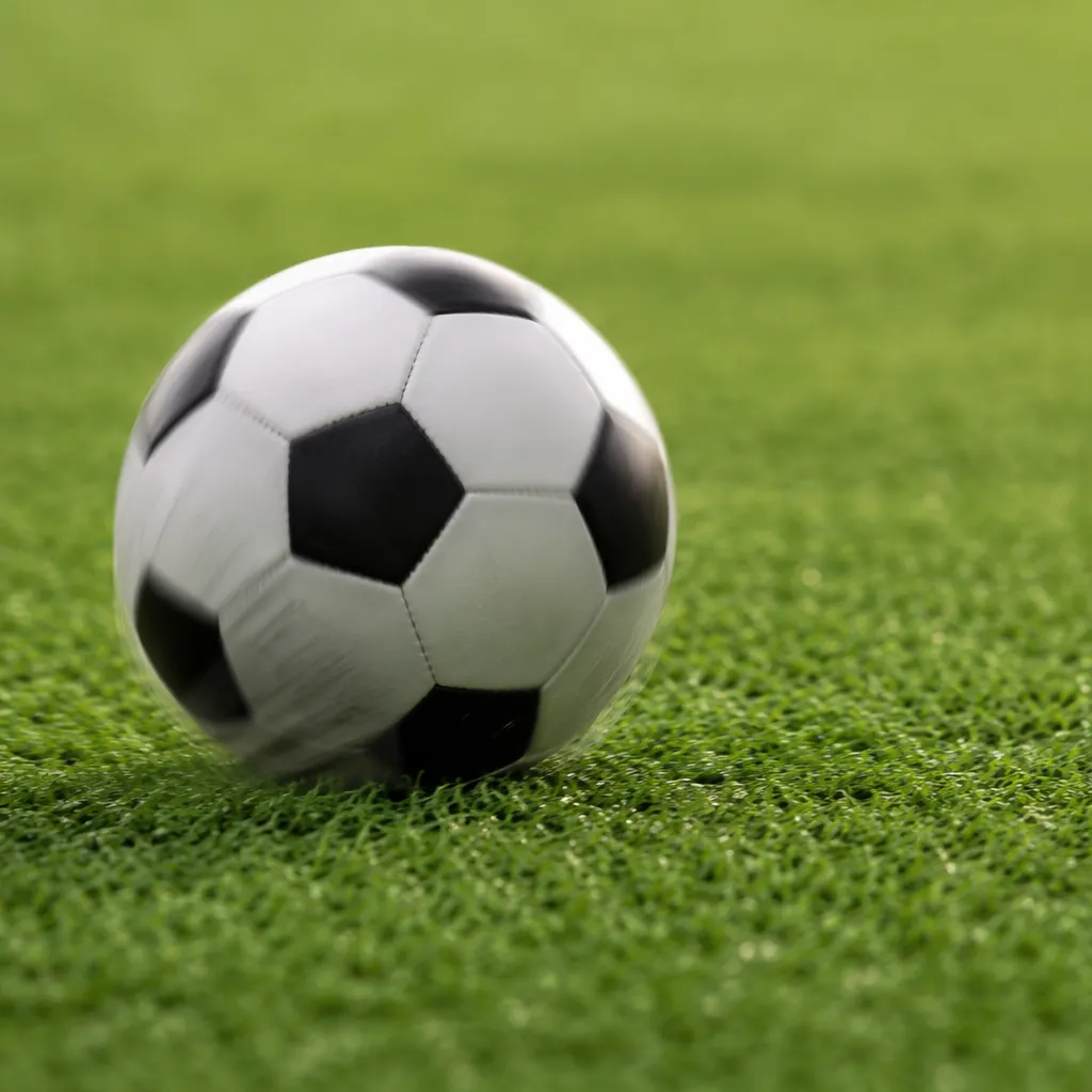 Close up of a soccer ball rolling on a perfectly manicured grass pitch, soft nat