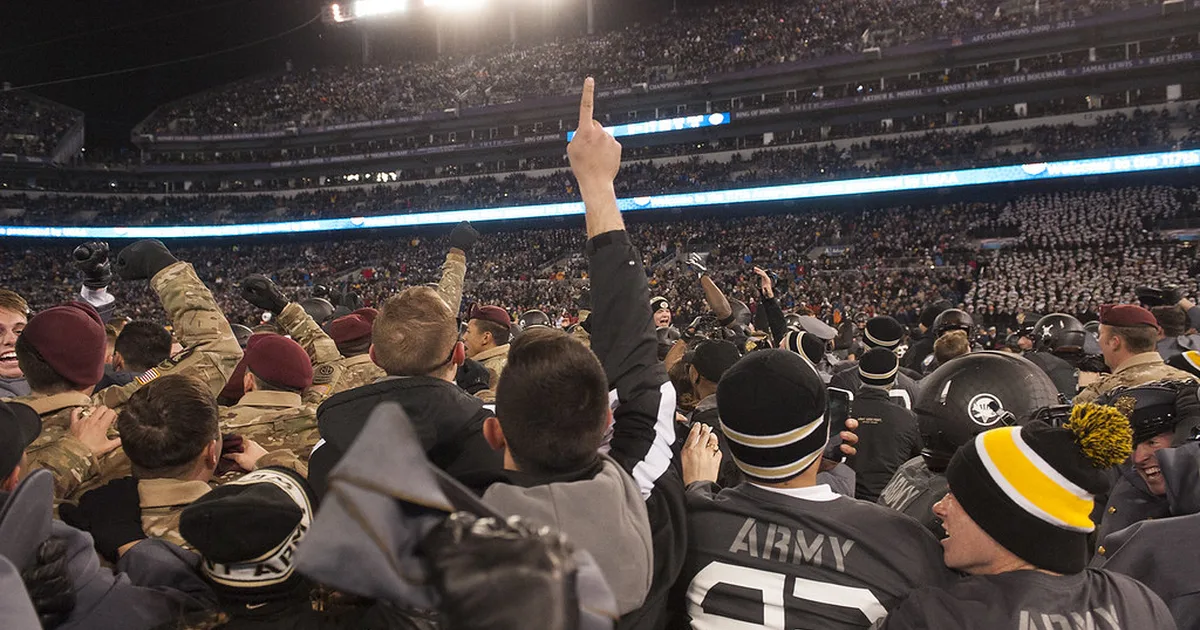 A wide shot of a diverse group of football fans cheering in a stadium stand, holding color