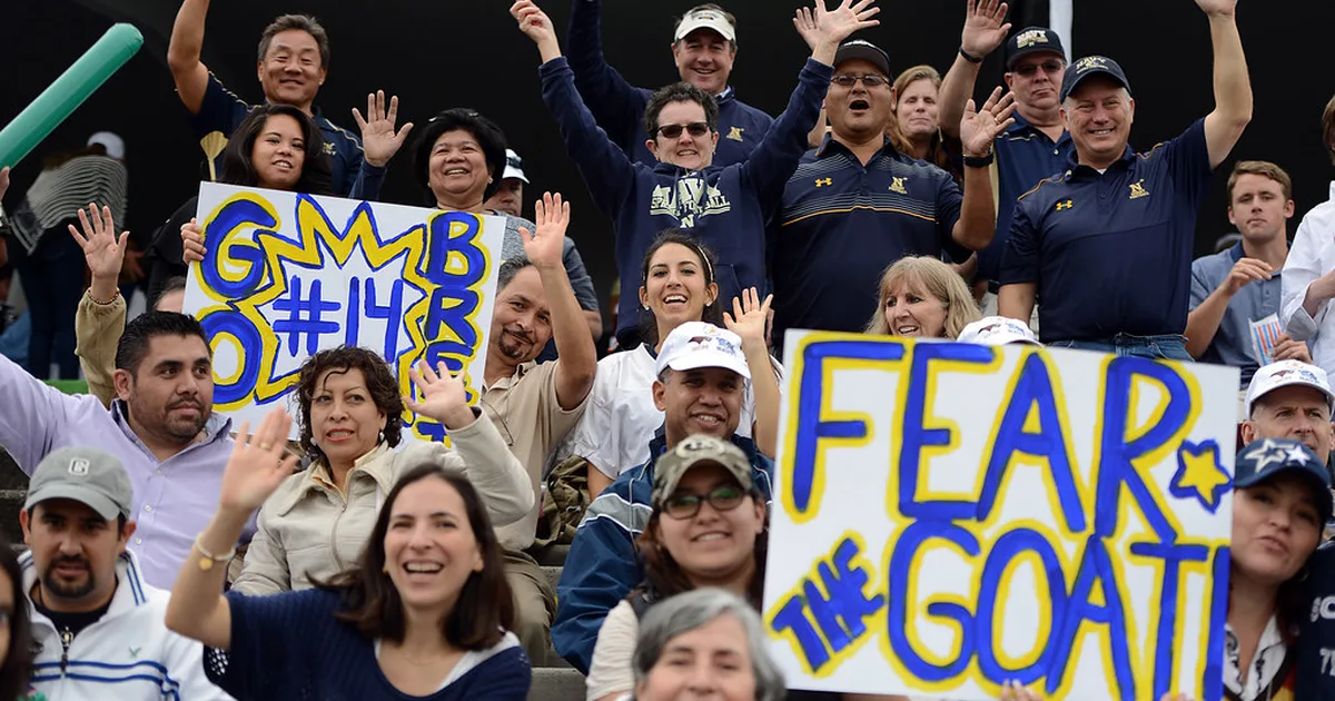 Wide shot of a modern football stadium at dusk, with colorful stadium lights on, blurred c
