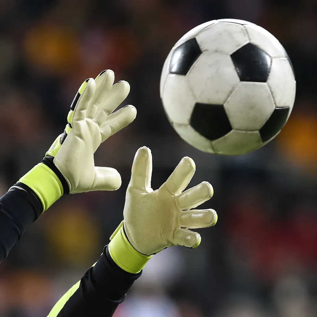 Close-up shot of goalkeeper gloves reaching to catch a flying soccer ball, blurr