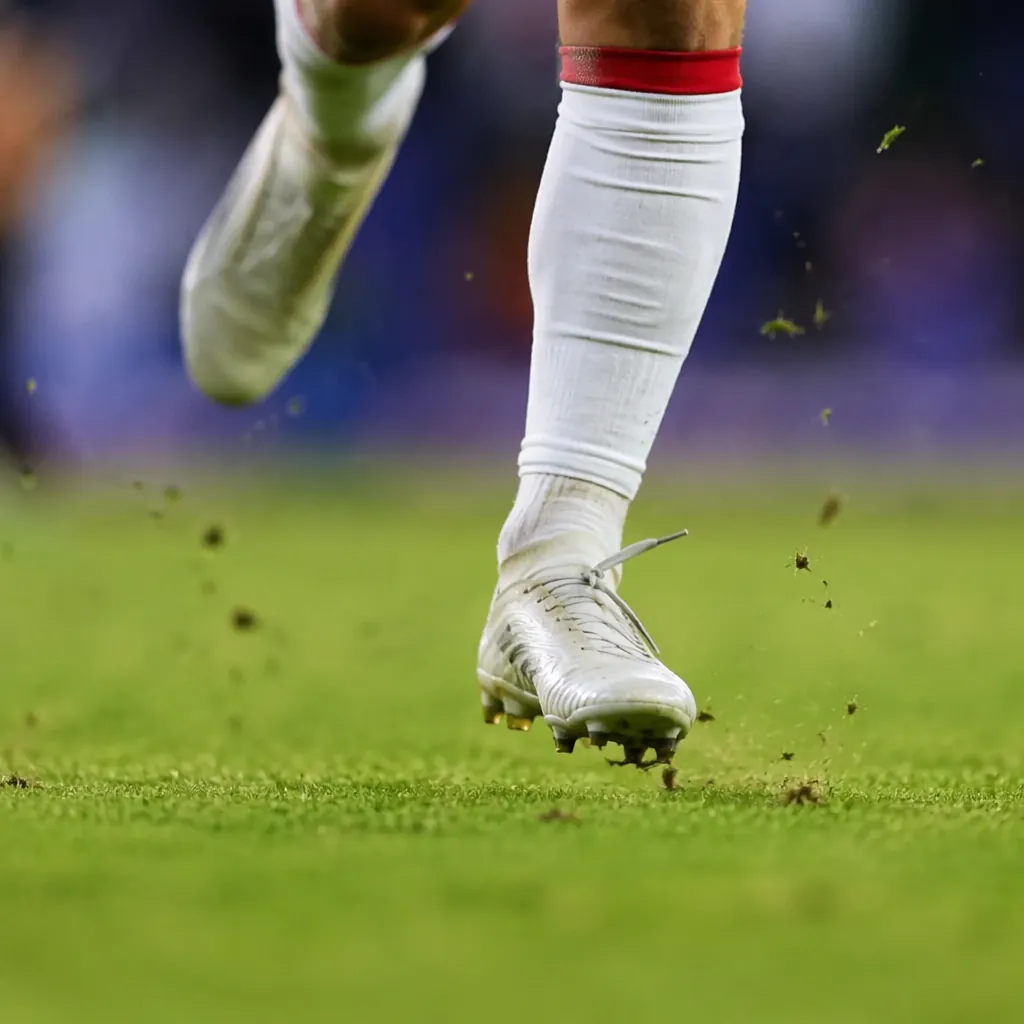 Close-up of a soccer player's feet running on grass with motion blur, bright sta