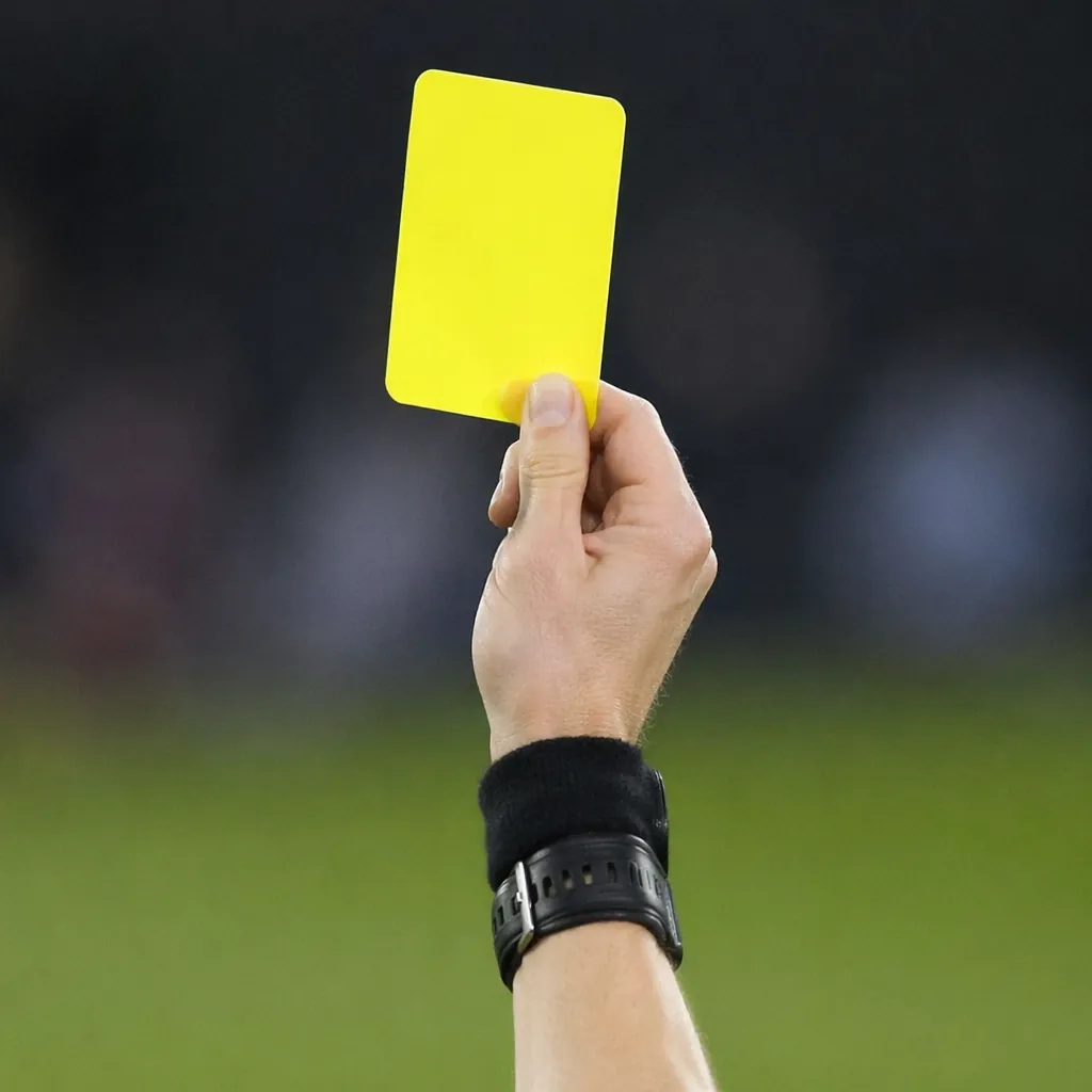 Close-up of a yellow referee card held up by a referee's hand, blurred backgroun