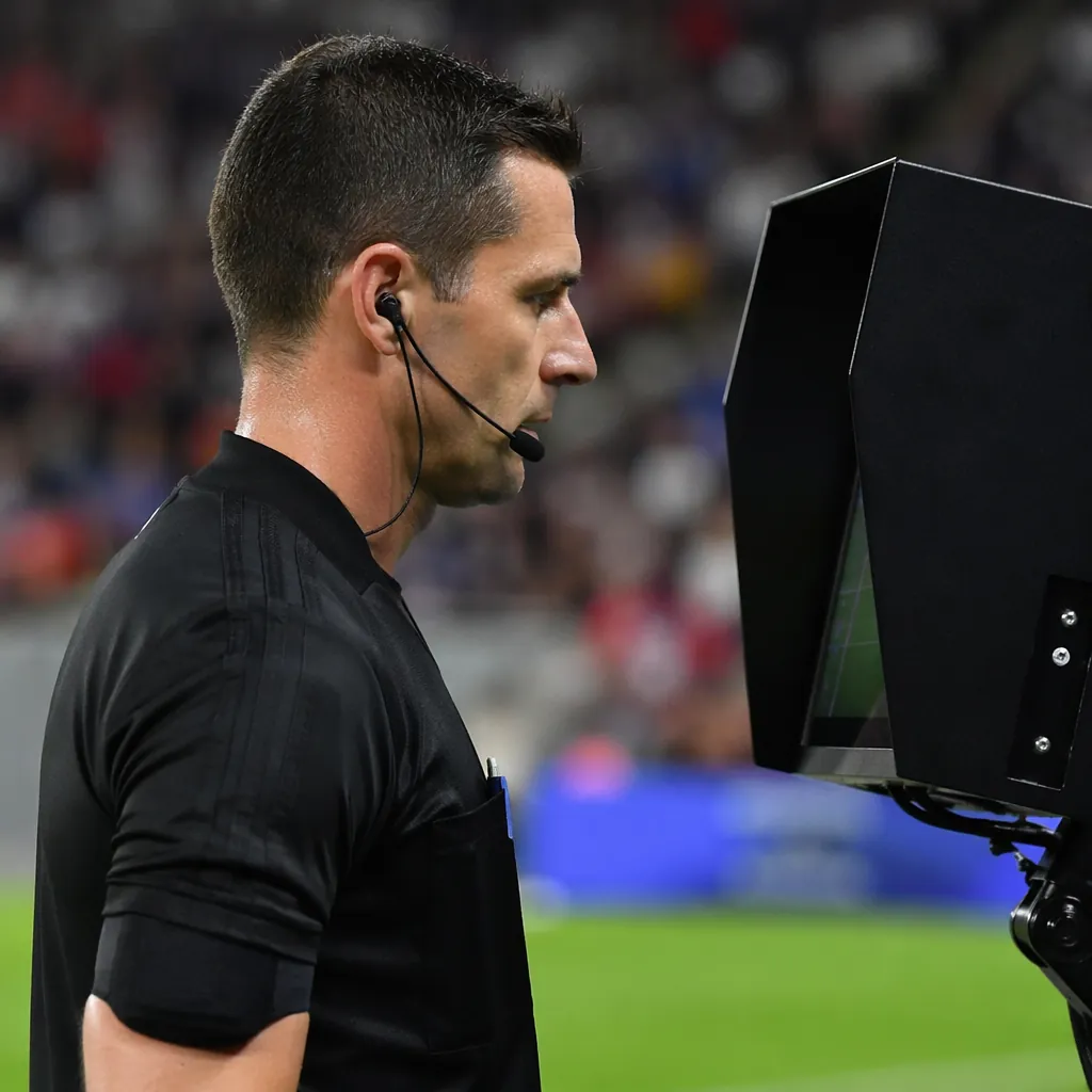 Close-up of a football referee in black uniform checking a VAR monitor on the si