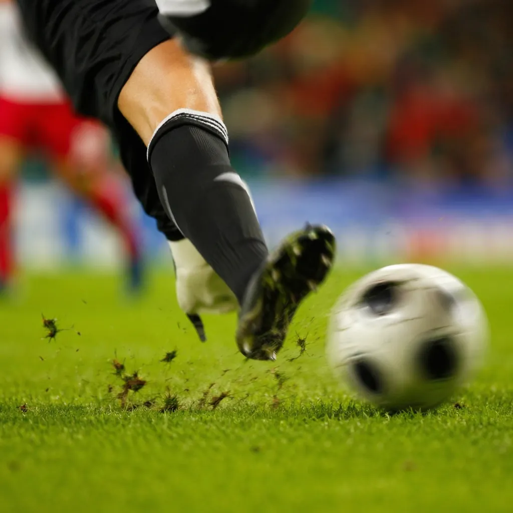 Dynamic action shot of a football player's feet kicking a ball on grass, motion 