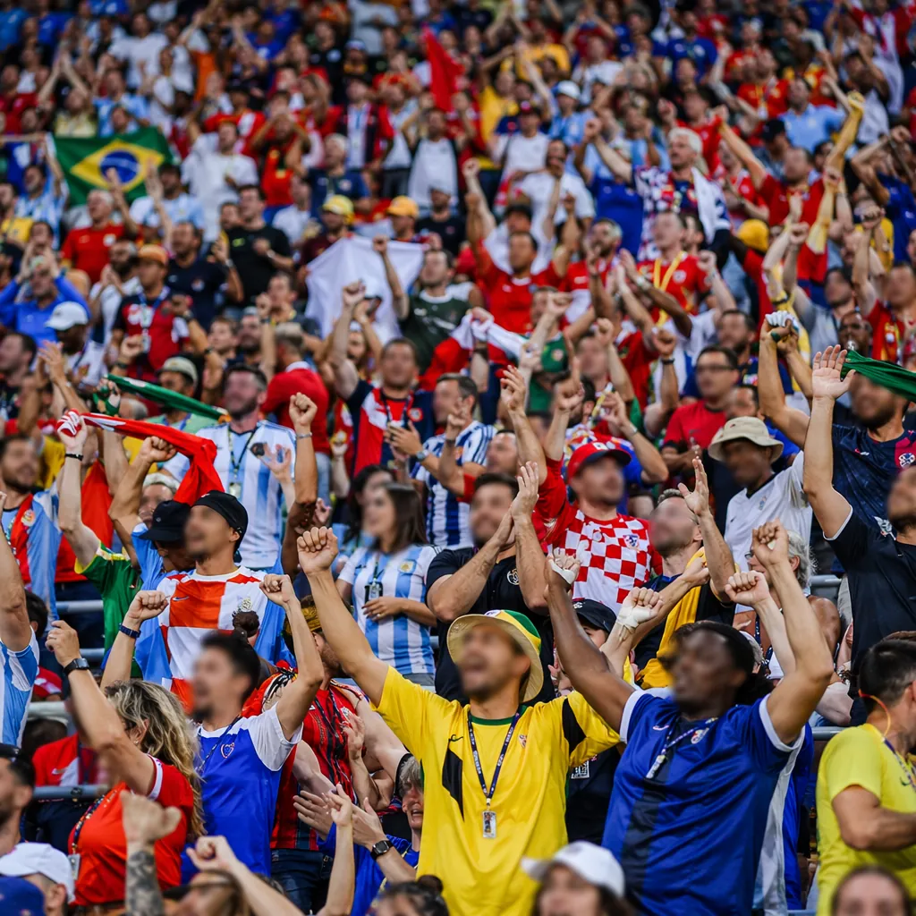 Wide shot of diverse soccer fans celebrating in stadium stands, wearing mixed na