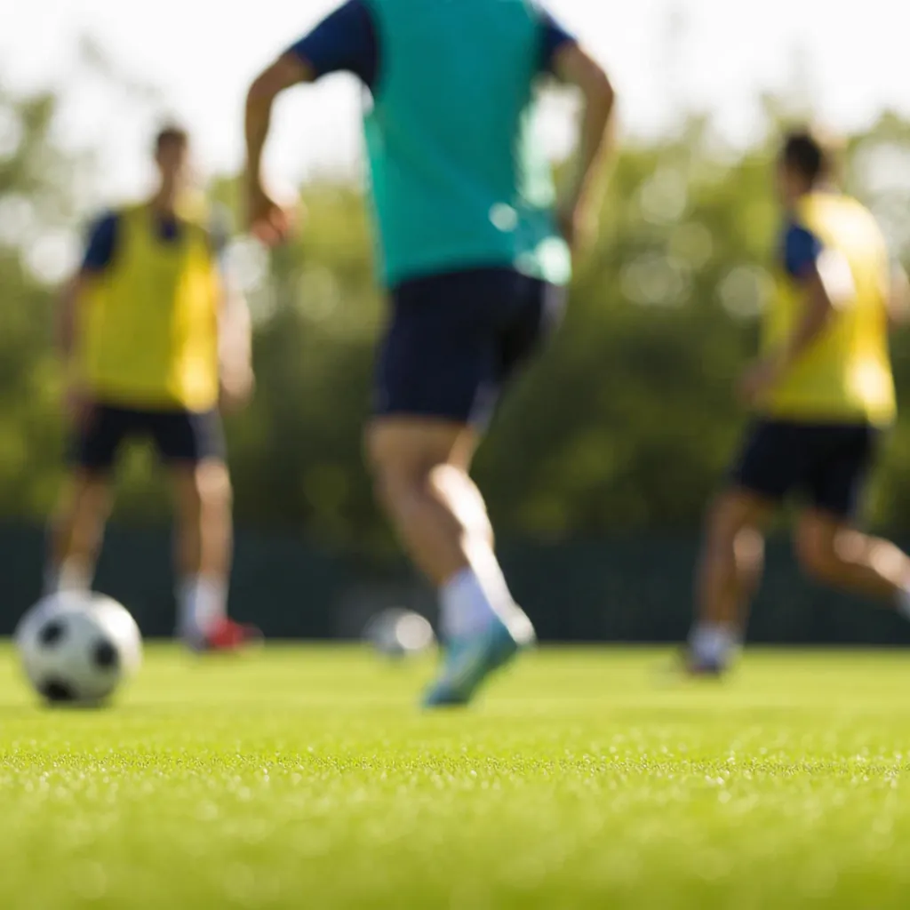 Blurred shot of football players training on a green pitch under bright sunlight