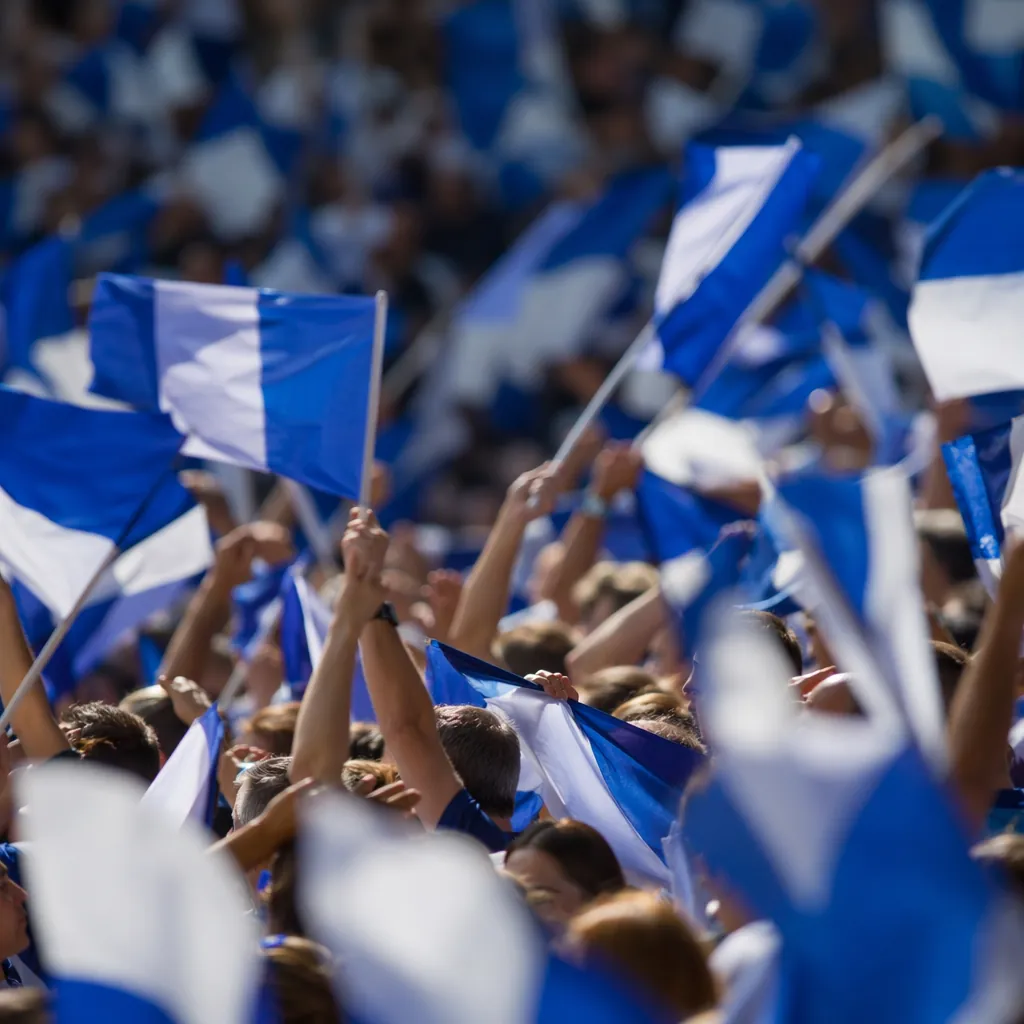 Blurred English football fans waving blue and white flags in stadium stands, che