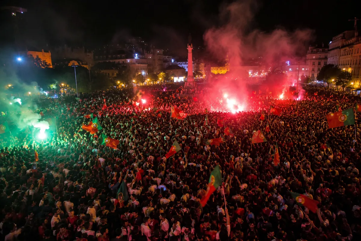 Wide shot of a massive crowd of football fans celebrating in a city square at night, wavin