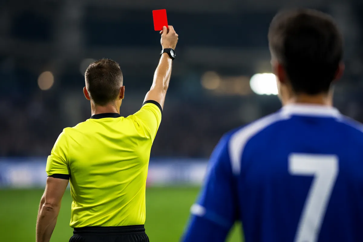 Professional editorial sports photography of a football referee holding up a red card to a