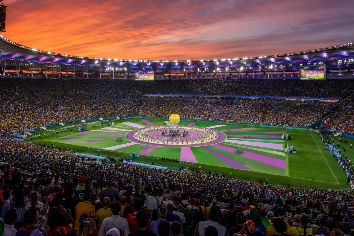 Wide shot of a packed World Cup final stadium at dusk, bright stadium lights illuminating