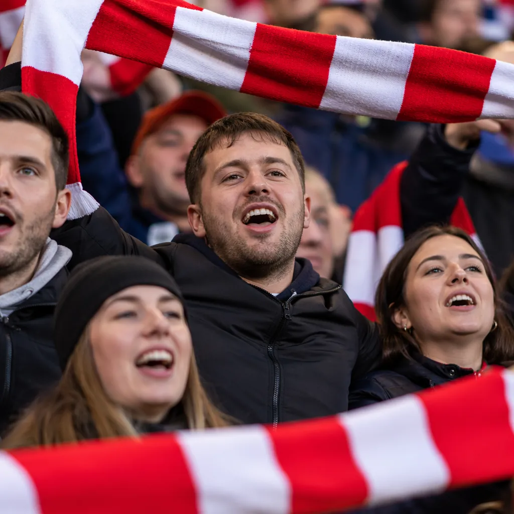 Close up candid shot of football fans singing together in stadium stands, holdin