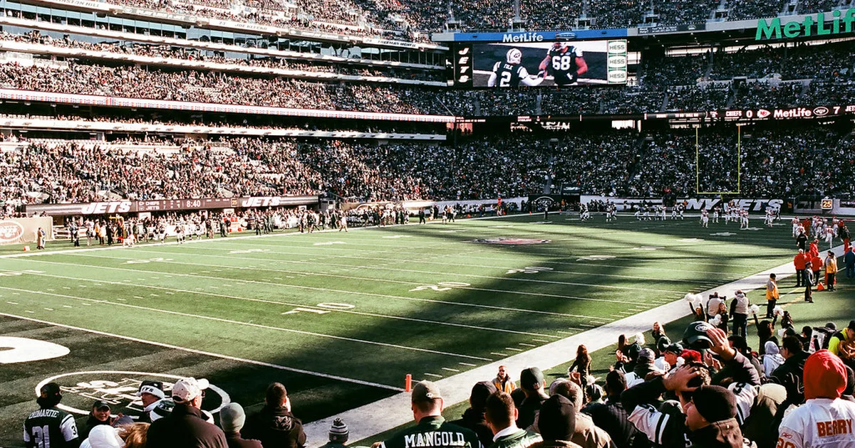 Wide shot of a modern football stadium during golden hour, empty green pitch visible, brig