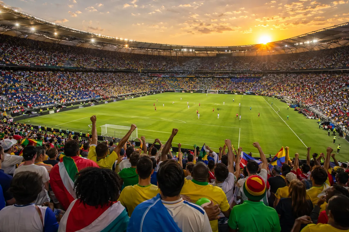 Wide shot of a generic outdoor soccer stadium at golden hour, packed with cheering fans in