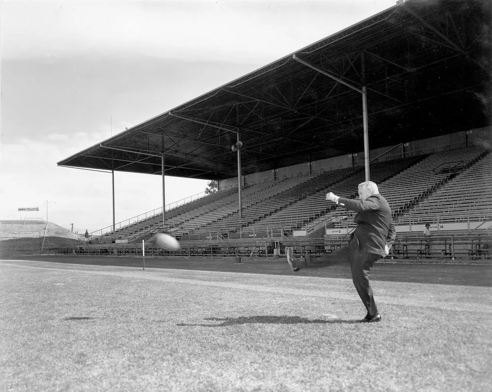Wide shot of a football pitch during match time, blurred cheering fans in the st