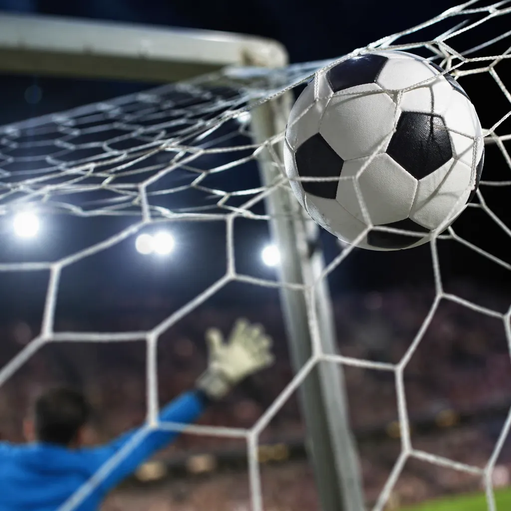 Close up shot of a football flying into the top corner of a goal net, goalkeeper