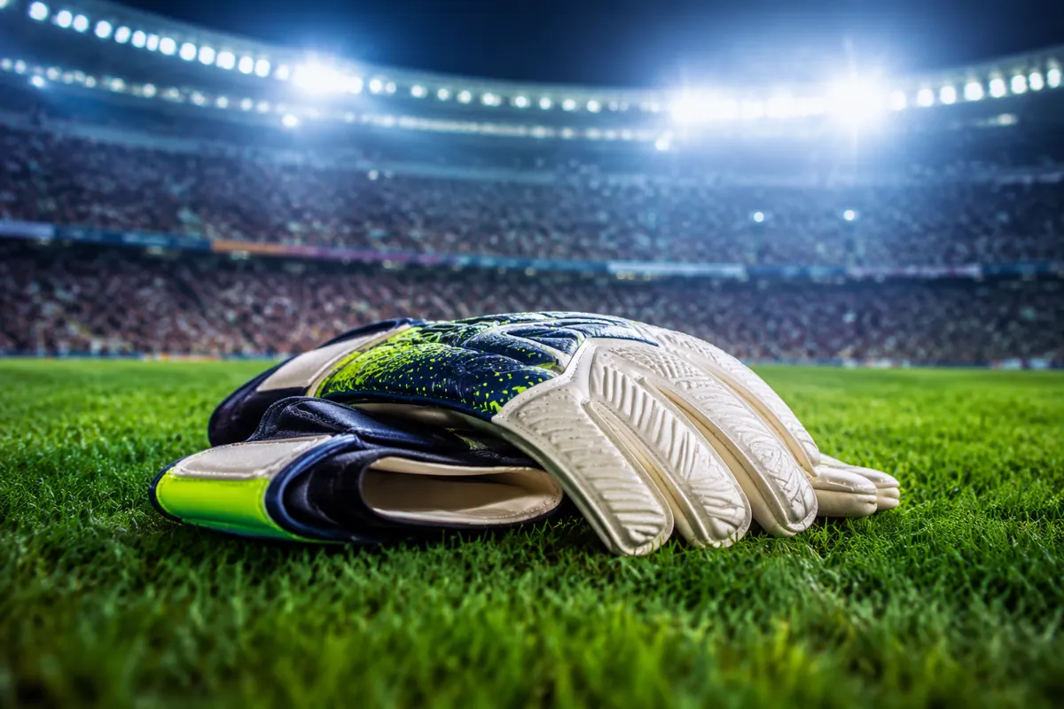 Professional football editorial header image, close-up of goalkeeper gloves resting on a w