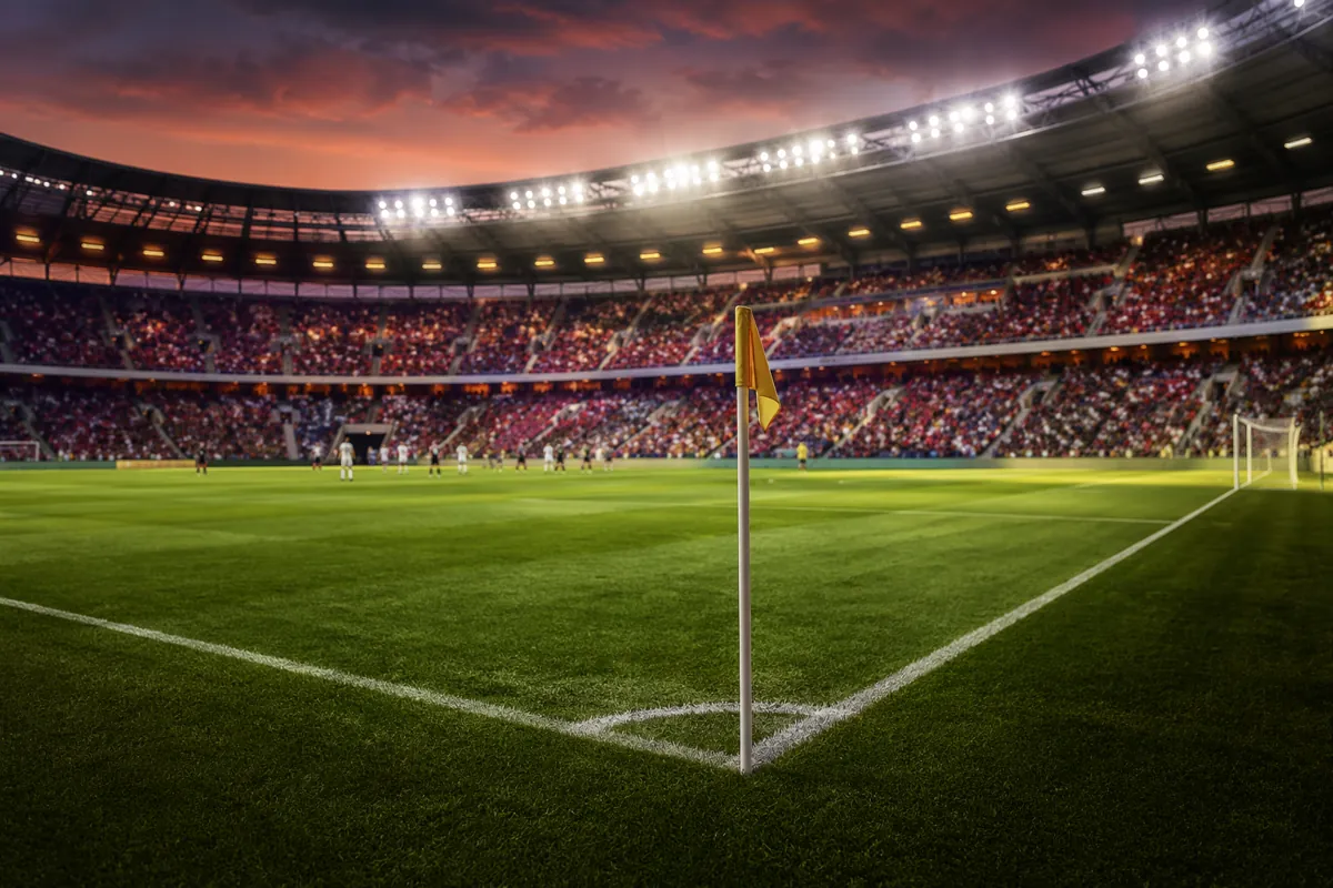 Professional soccer field under bright stadium lights at dusk, blurred crowd of fans in th