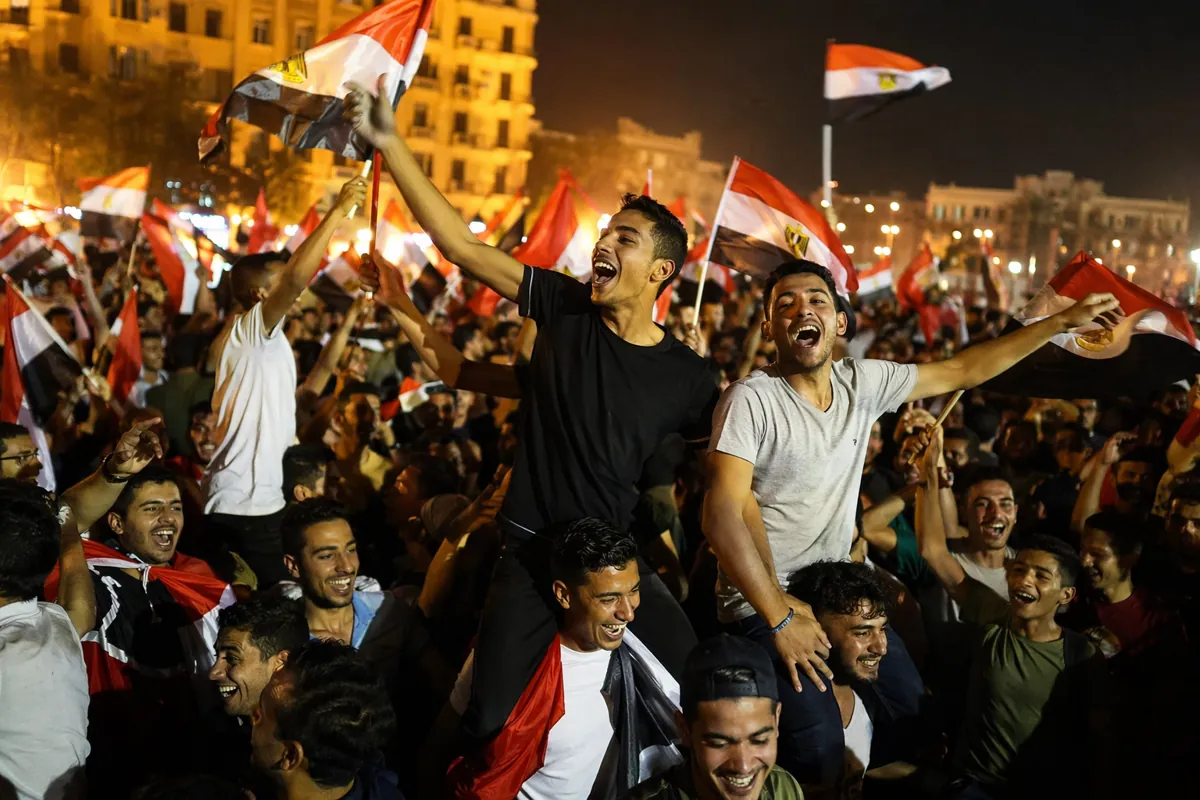 Vibrant night street scene in Cairo, thousands of joyful Egyptian fans waving national fla