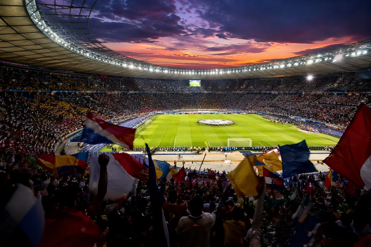 Wide shot of a packed modern football stadium at dusk, vibrant stadium lights illuminating