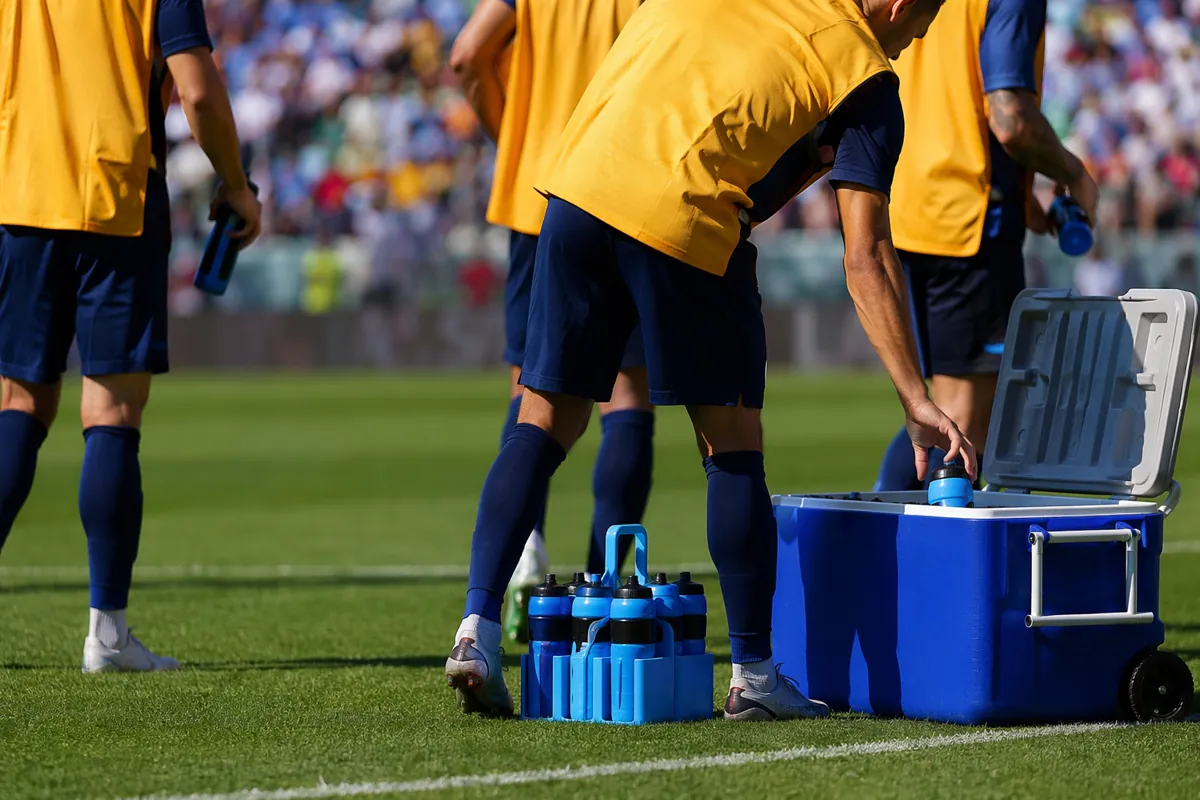 Professional football match sideline scene, blurred player figures taking water from coole