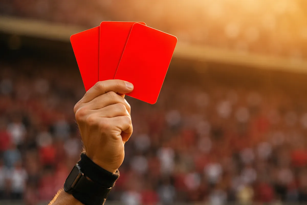 Close up of a referee holding three red cards against a blurred football stadium backgroun
