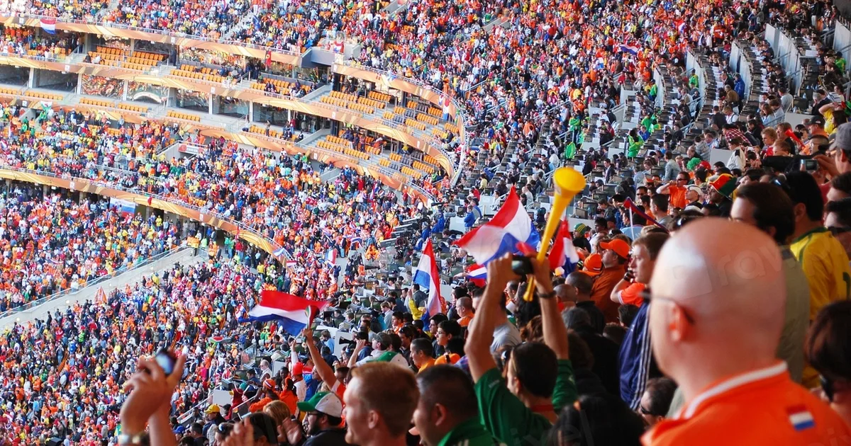 Vintage football stadium at dusk, blurred crowd of cheering fans in stands, soft golden li