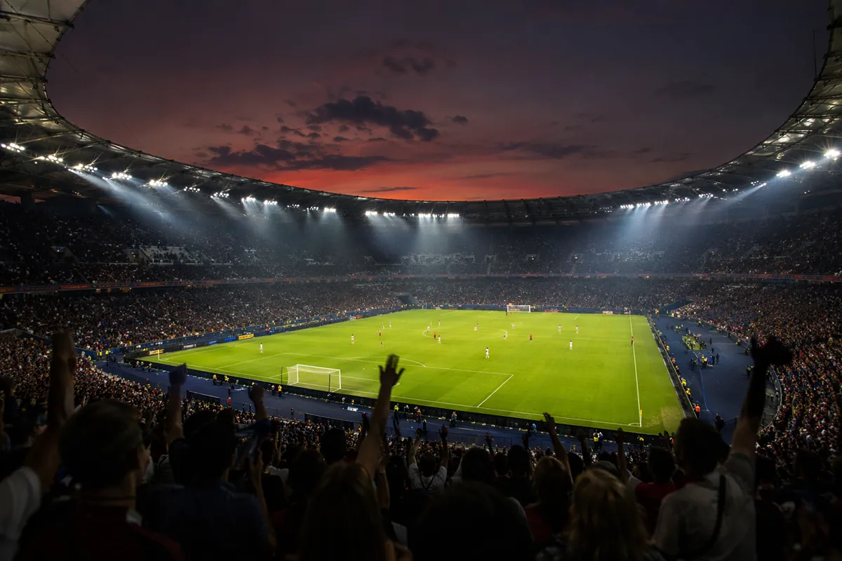 Wide shot of a modern FIFA World Cup football stadium at dusk, bright floodlights illumina