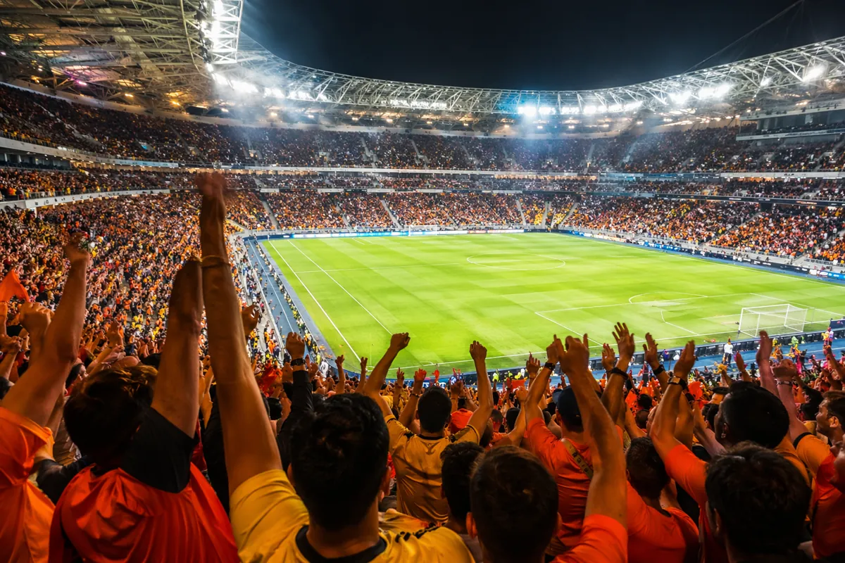 Professional sports news header image, vibrant orange and blue football stadium atmosphere