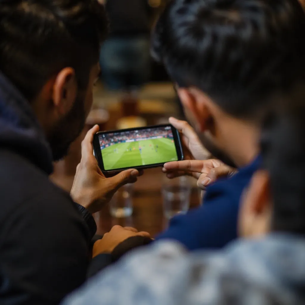 Small group of people gathered around a mobile phone watching a football stream,