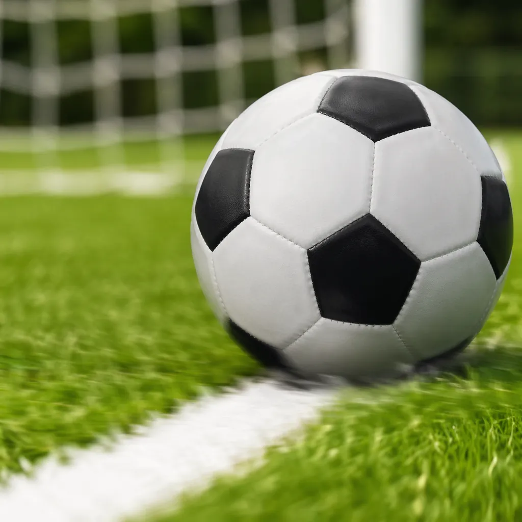 Close up of a football rolling across green grass near the goal line, blurred wh