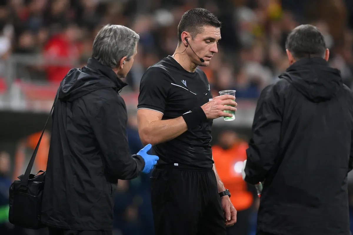 Professional soccer match scene, referee standing on grass sideline holding a transparent