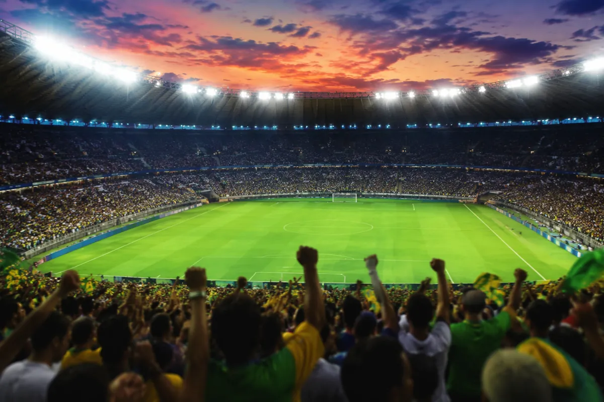 Professional football stadium at dusk, bright stadium lights, empty green pitch, blurred c
