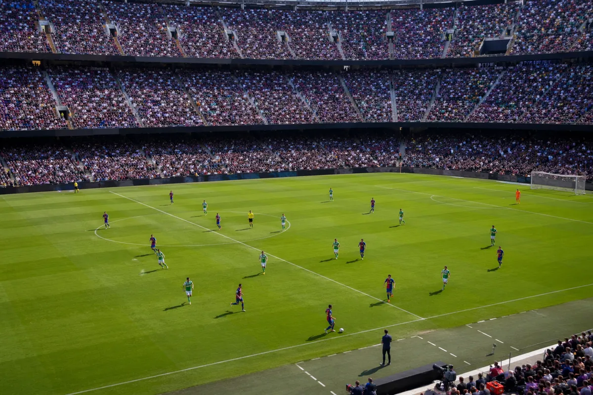 Wide shot of a professional football stadium during a friendly match, players in blue-red