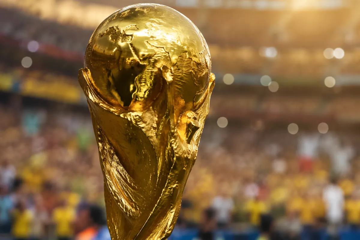 Close up of a golden FIFA World Cup trophy with a blurred background of a packed football