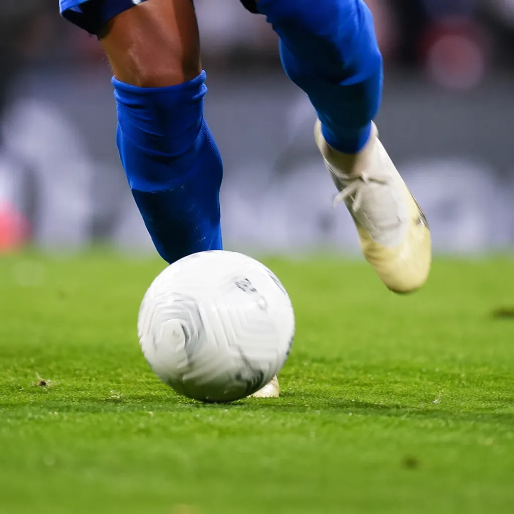 Close-up shot of a football player's boots dribbling a white football on well-ma